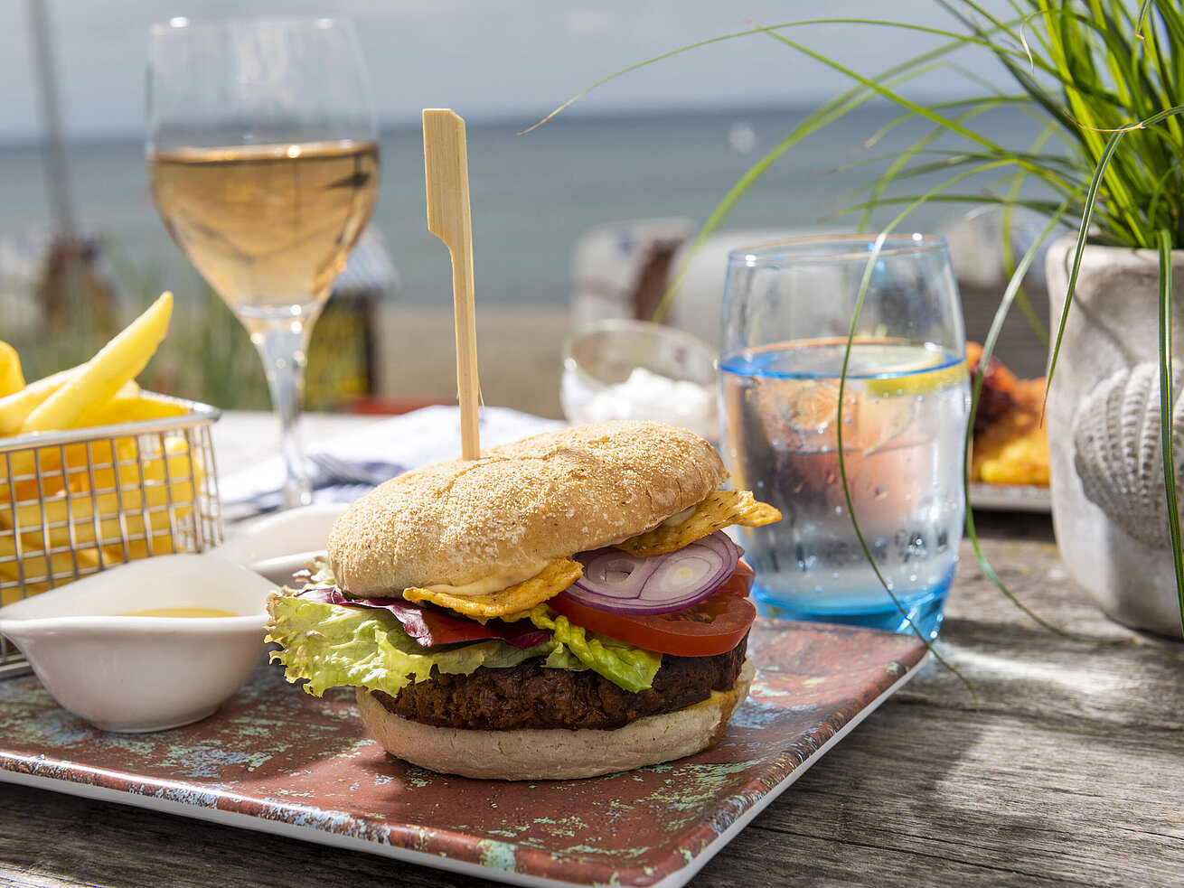 Burger avec frites, salade et boissons sur une table en bois dans le Beach-Lounge du Maritim Hotel Timmendorfer Strand.