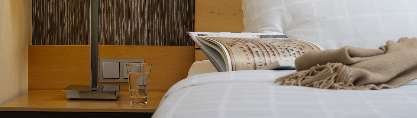 Gros plan d'une table de chevet au Maritim Hotel Düsseldorf avec une lampe, un verre d'eau et un livre sur le lit.