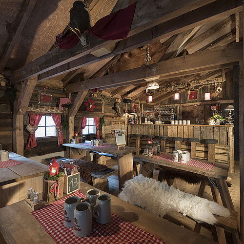 Rustikale Bar und festlich gedeckte Holztische mit roten Vorhängen in der ElbAlm