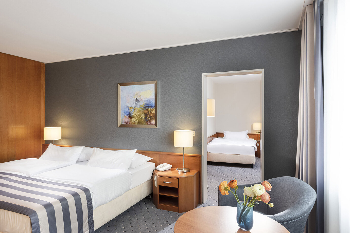 Camera familiare al Maritim Hotel Ulm con letto matrimoniale, zona salotto e parete a specchio elegante