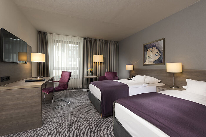 Chambre double moderne de l'hôtel Maritim Königswinter avec deux lits, bureau et décoration élégante.