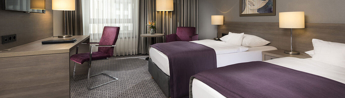 Chambre double moderne de l'hôtel Maritim Königswinter avec deux lits, bureau et décoration élégante.