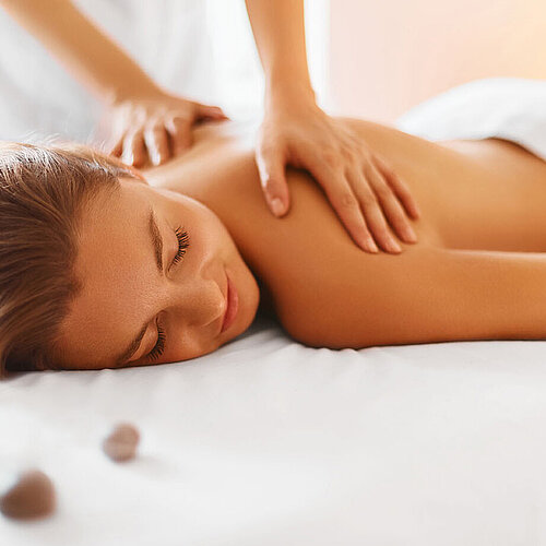 Woman enjoying relaxing back massage in spa with warm light and stones
