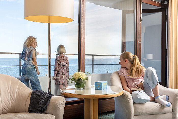 Les enfants profitent de la vue sur la mer depuis la suite familiale, tandis qu'une fillette lit dans un fauteuil.