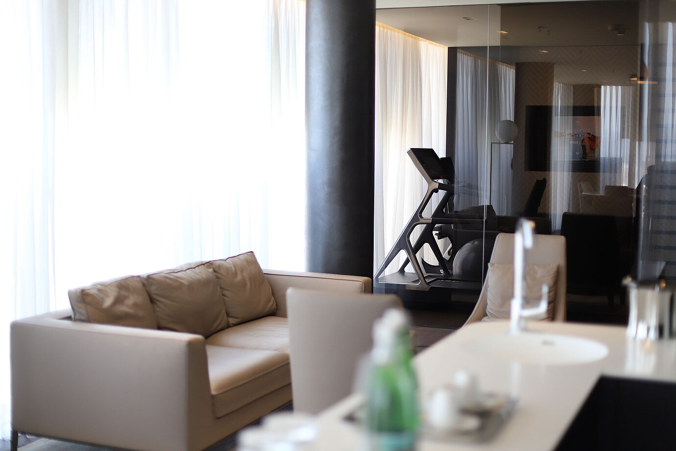 Coin salon avec canapé beige et vue sur la salle de sport avec tapis roulant au Maritim Hotel Plaza Tirana