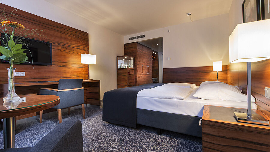 Chambre d'hôtel meublée au Maritim Hotel Munich avec lit confortable, espace de travail, TV et boiseries.