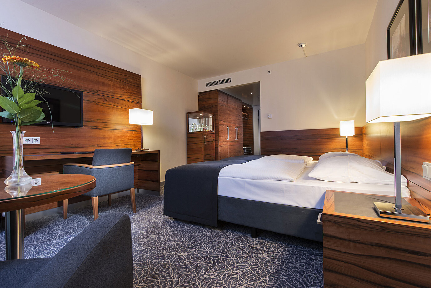 Camera d'albergo arredata presso il Maritim Hotel Monaco con letto confortevole, area lavoro, TV e pannelli in legno.