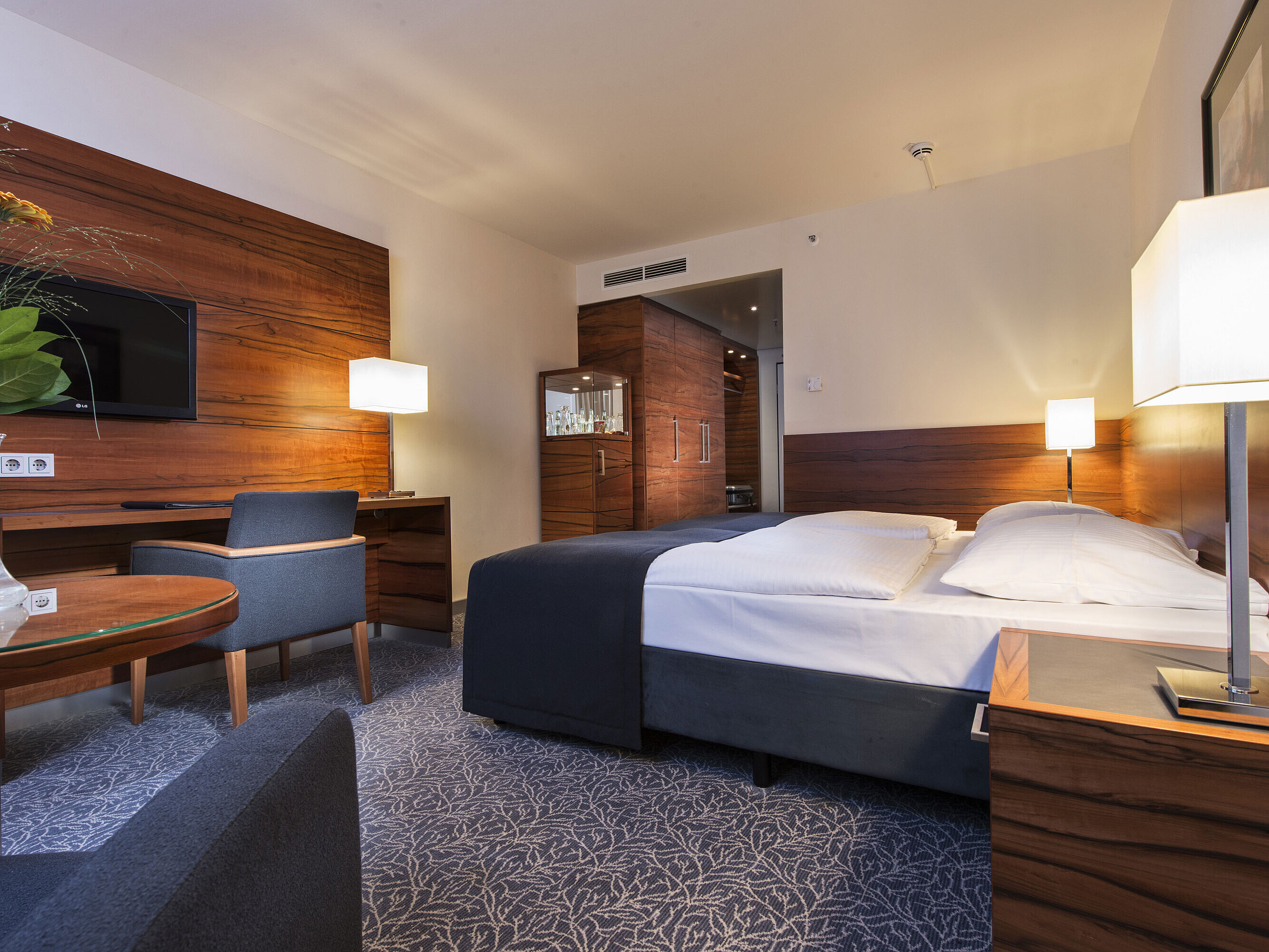Chambre d'hôtel meublée au Maritim Hotel Munich avec lit confortable, espace de travail, TV et boiseries.
