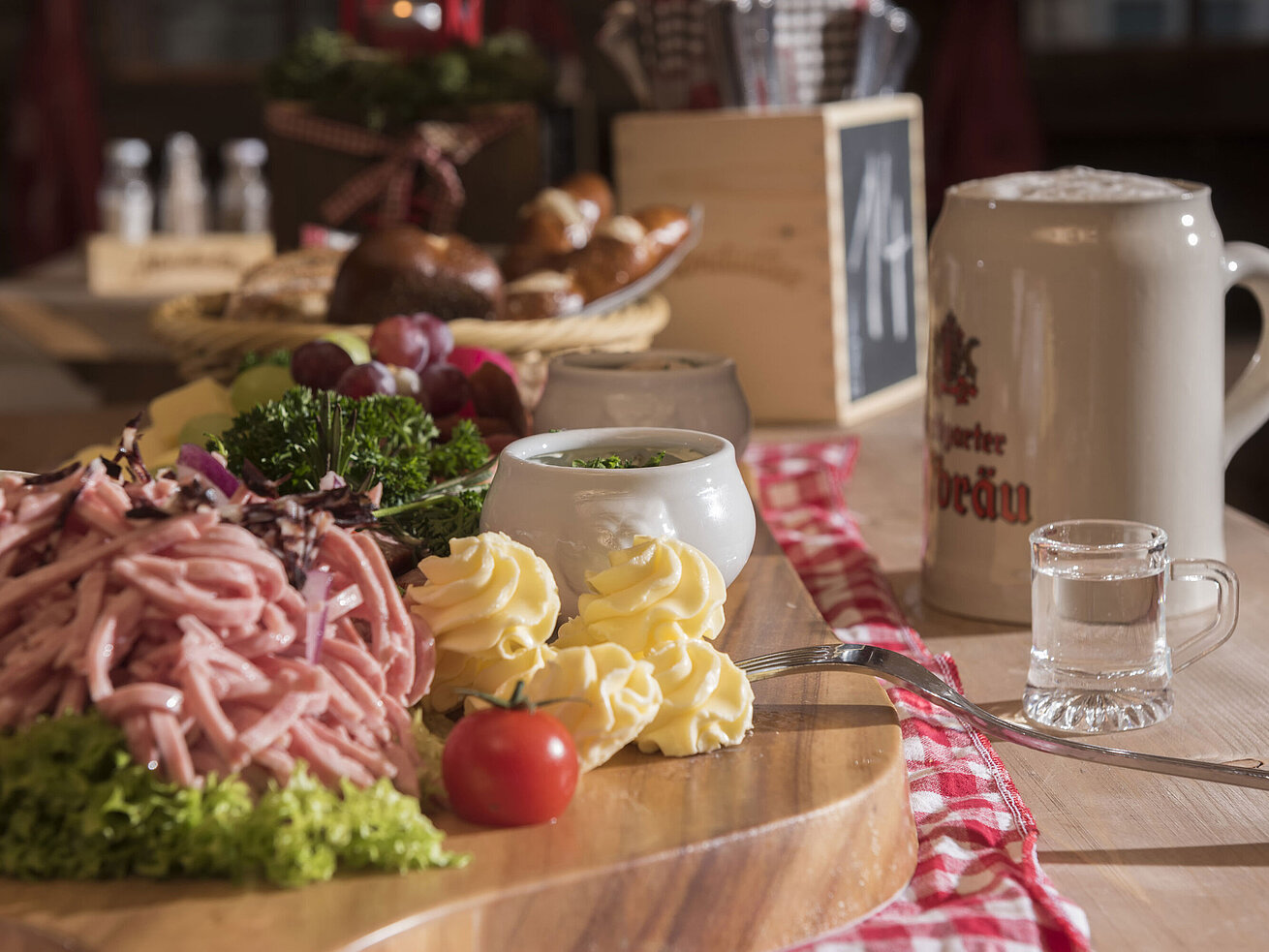 Bavarian sausage salad, butter rosettes, grapes and beer mug on a wooden board at Maritim Alm