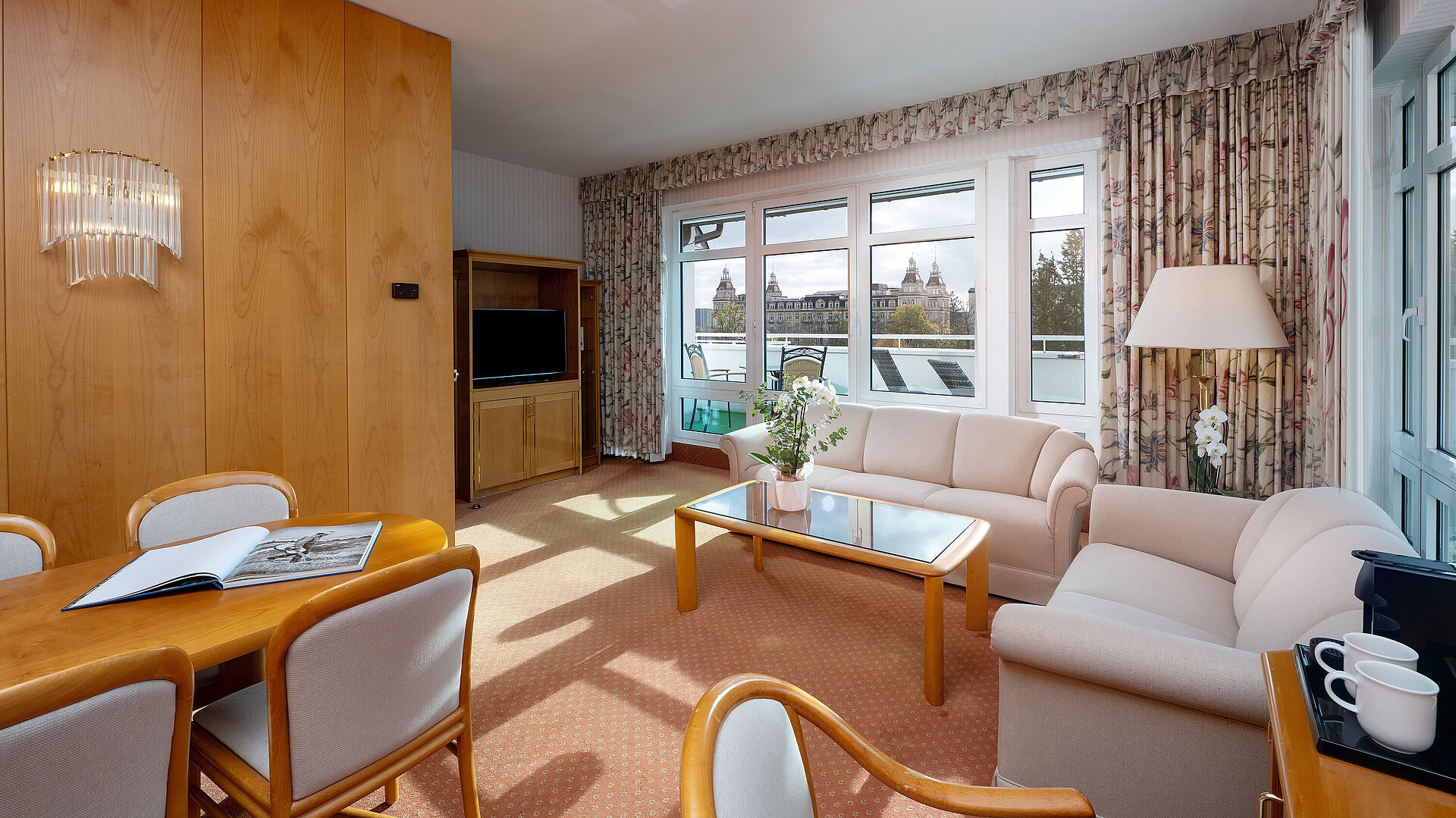 Junior Suite with bright living area, sofa, large window, dining space and classic interior at the Maritim Hotel.