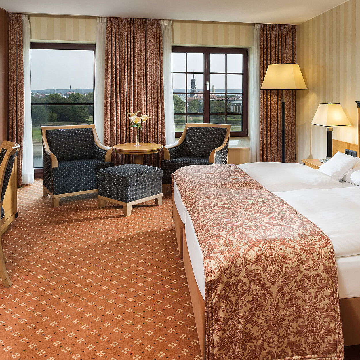 Habitación superior en el Maritim Hotel Dresden con cama doble elegante, escritorio y zona de estar con vistas a la ciudad.