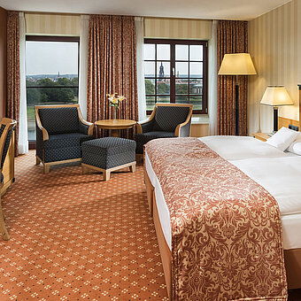Habitación superior en el Maritim Hotel Dresden con cama doble elegante, escritorio y zona de estar con vistas a la ciudad.