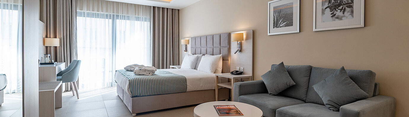 Spacious Junior Suite at Maritim Antonine Hotel & Spa Malta with a combined living and sleeping area, sofa and comfortable double bed.