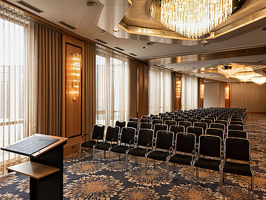 Grande salle de conférence avec sièges en rangée, pupitre et lustres à l’hôtel Maritim Ulm.