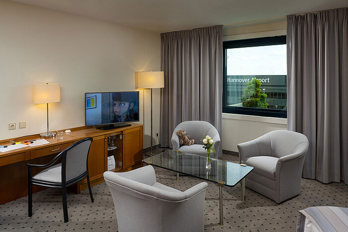 Camera familiare confortevole con area salotto, TV e vista sull’aeroporto di Hannover al Maritim Hotel Hannover.