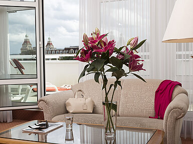 Soggiorno luminoso con fiori, divano e vista sulle torri dal balcone al Maritim Hotel Bad Wildungen