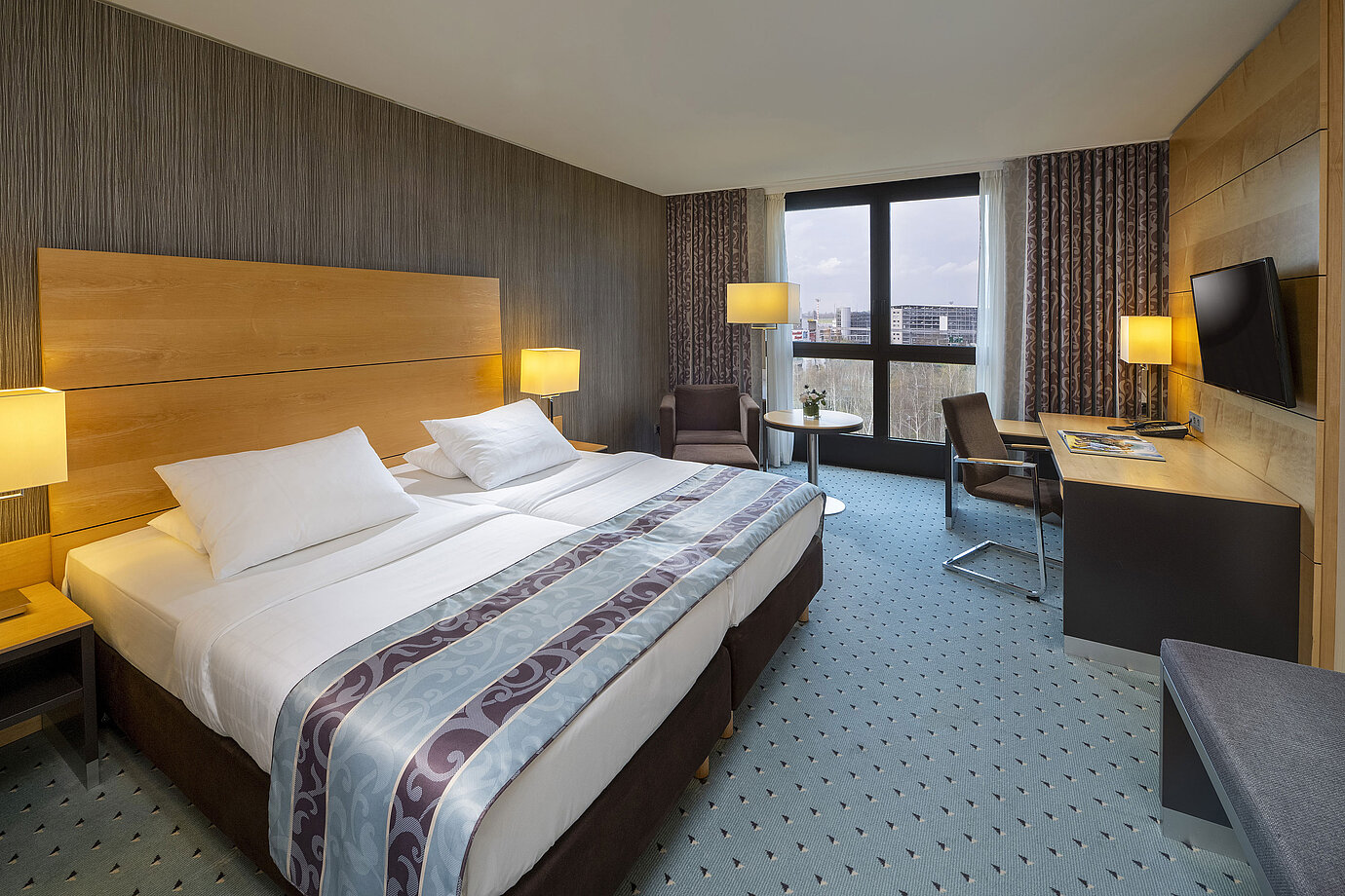 Chambre confort au Maritim Hotel Düsseldorf avec grand lit double, bureau, fauteuil et fenêtre panoramique.
