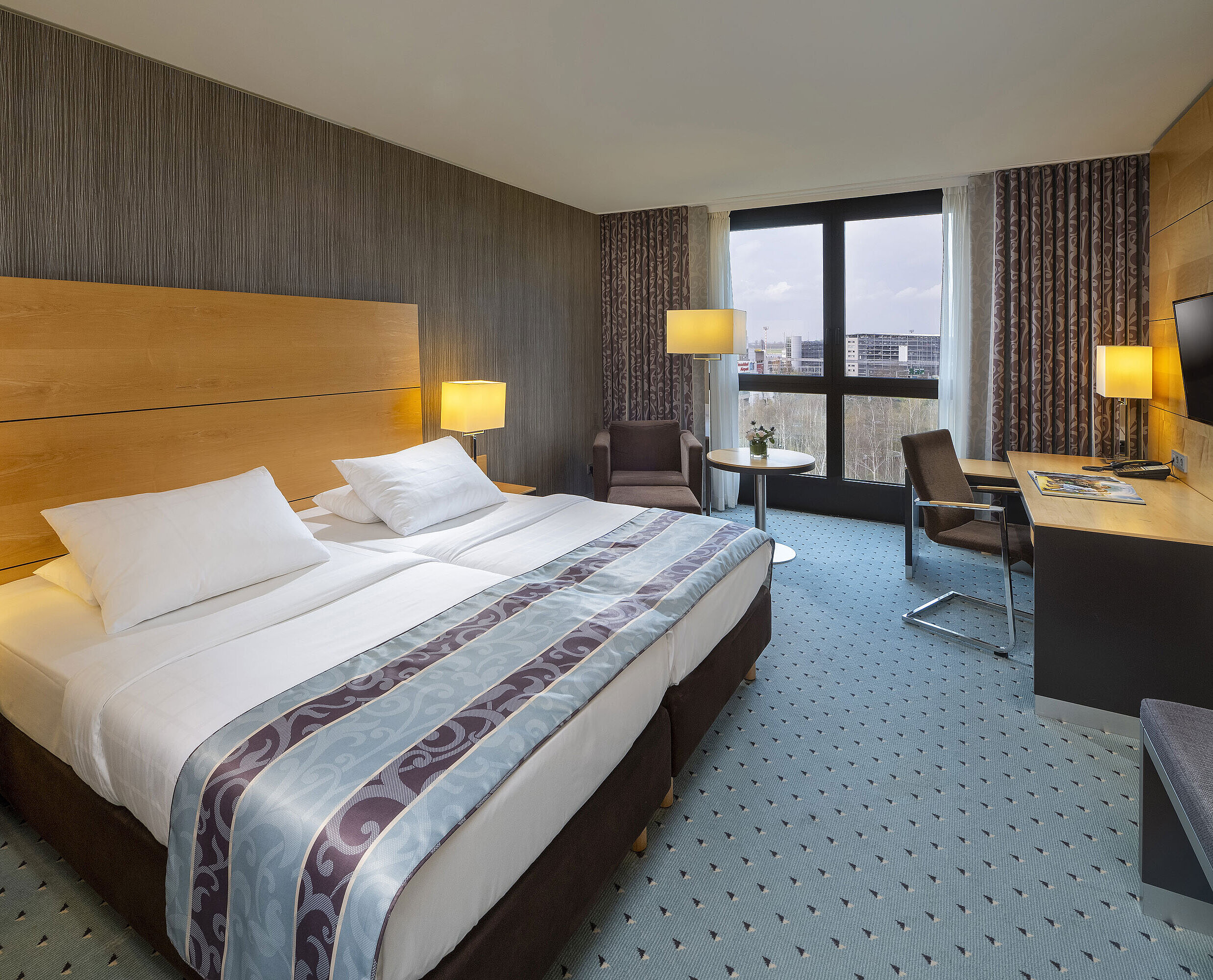 Comfort room Comfort room at Maritim Hotel Düsseldorf with a large double bed, desk, armchair, and panoramic window.