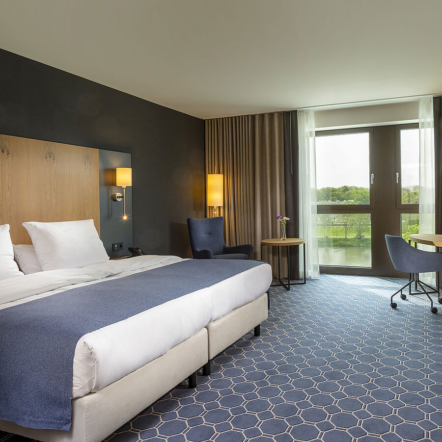 Spacious double room at Maritim Hotel Ingolstadt with large bed, desk, and a view of the river.