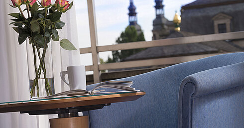  Detalle elegante de una habitación del Maritim Hotel Fulda con asiento azul, rosas y vistas a las torres barrocas de Fulda.