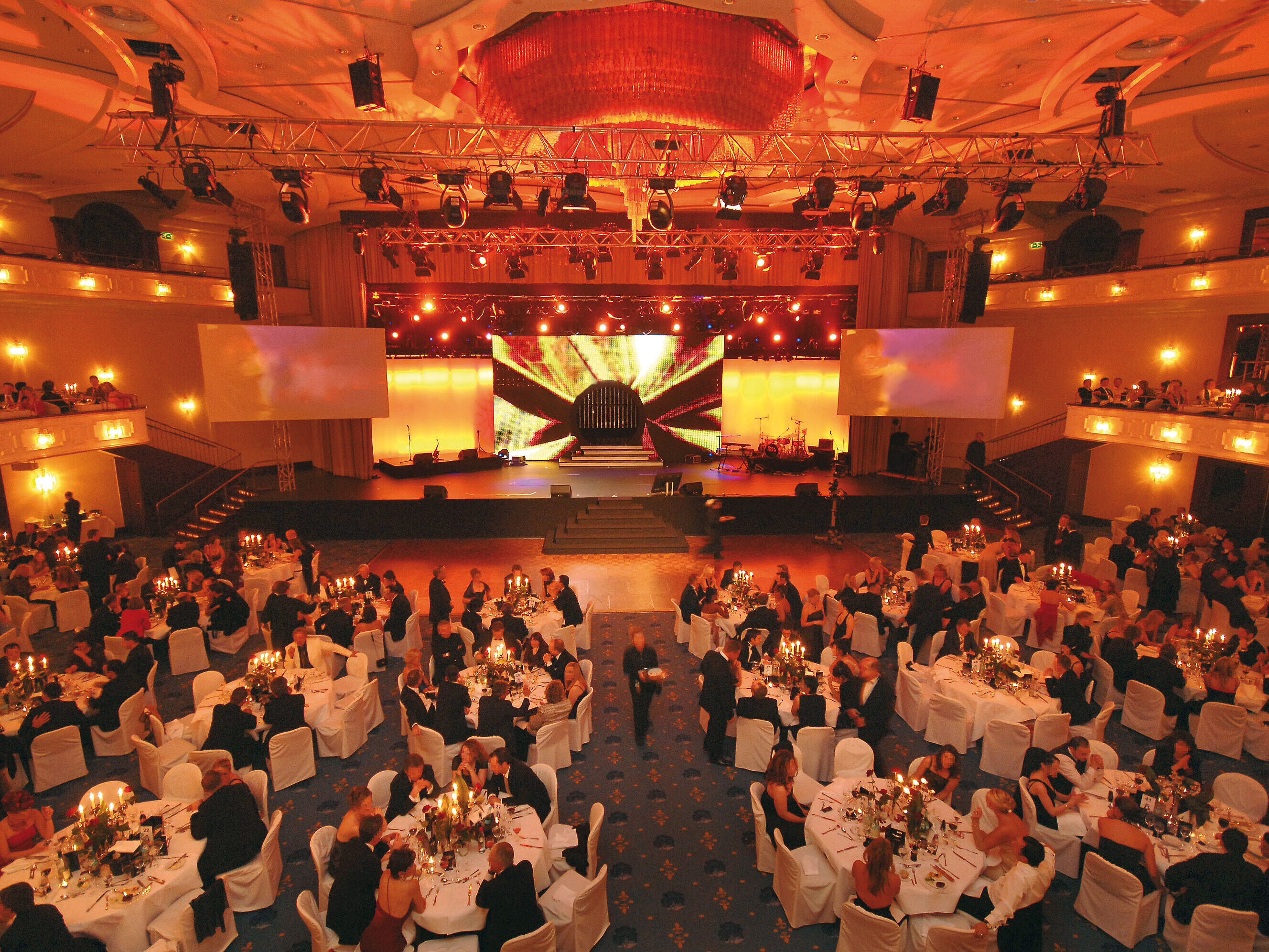 Sala de eventos iluminada festivamente en el Hotel Maritim Colonia con mesas elegantemente dispuestas y luces de escenario.