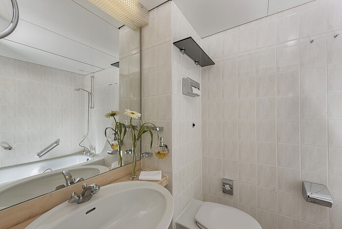 Salle de bain lumineuse au Maritim Hotel Bad Salzuflen avec douche, grand miroir et carrelage blanc