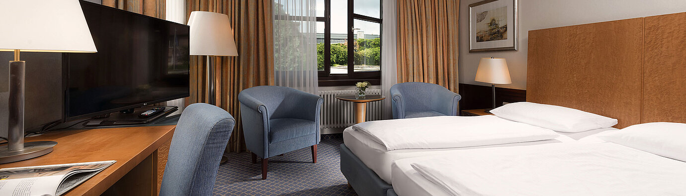 Chambre Classic au Maritim Hotel Fulda avec lit double confortable, bureau, coin salon et grande fenêtre.