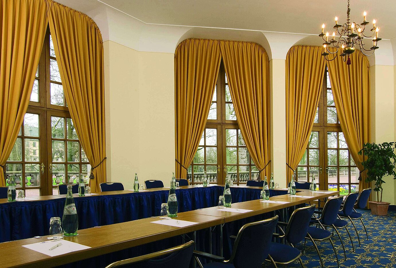 Sala de reuniones elegante con grandes ventanales, cortinas doradas y lámpara de araña en Maritim Hotel Fulda.