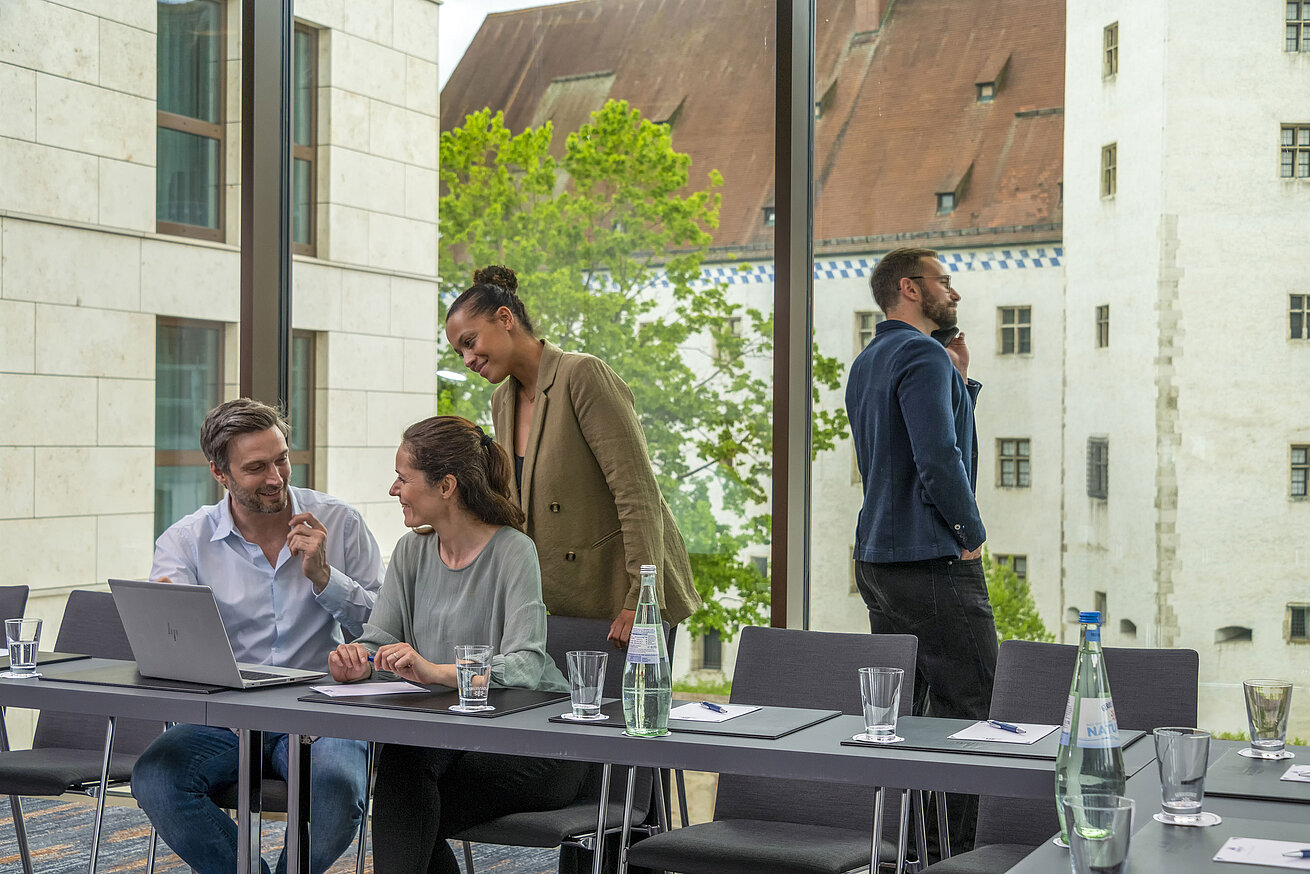 Professionnels souriants dans la salle de réunion de l'hôtel Maritim Ingolstadt avec vue sur des bâtiments historiques.