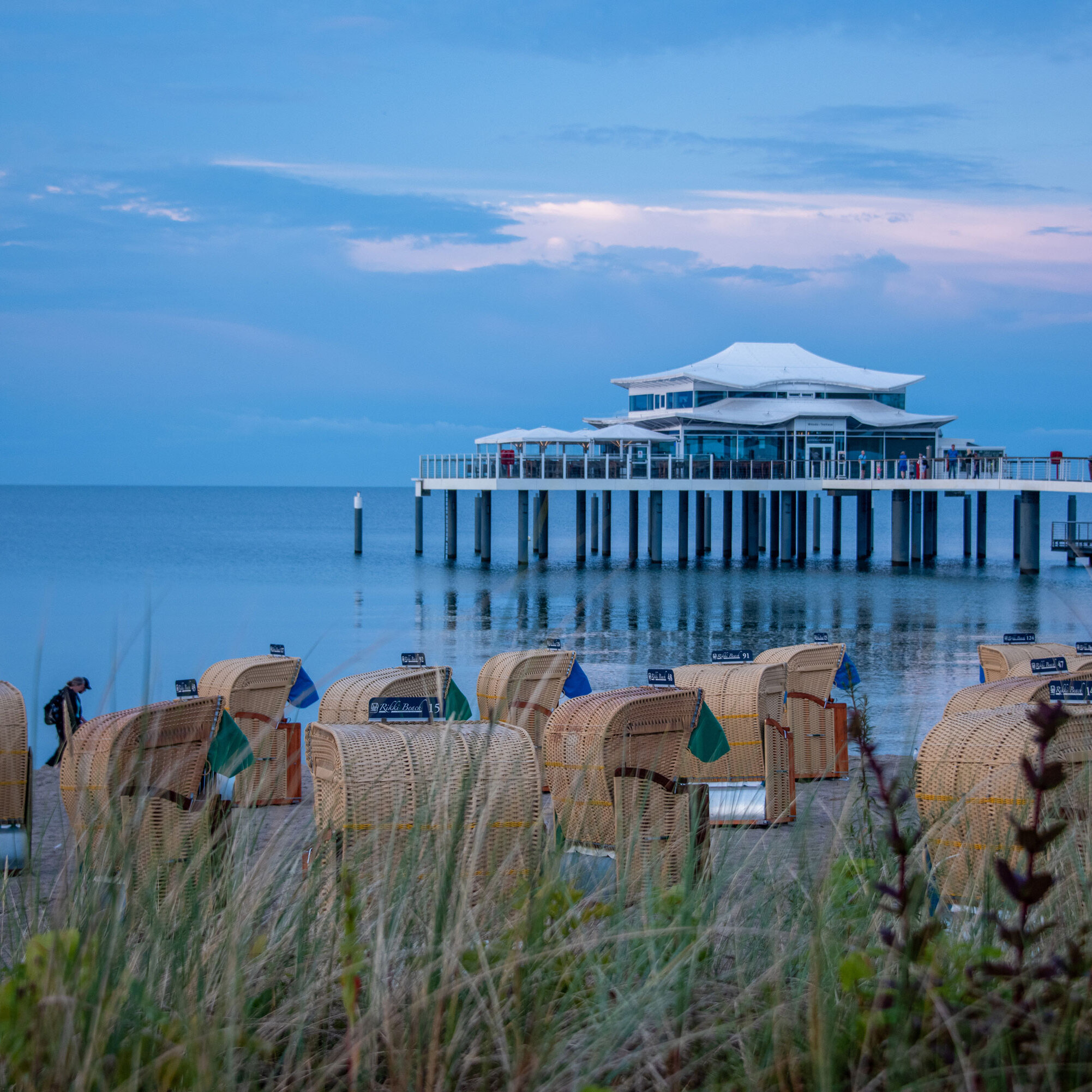 Beach chairs on the sandy shore with a view of the Baltic Sea and a pier at sunset.