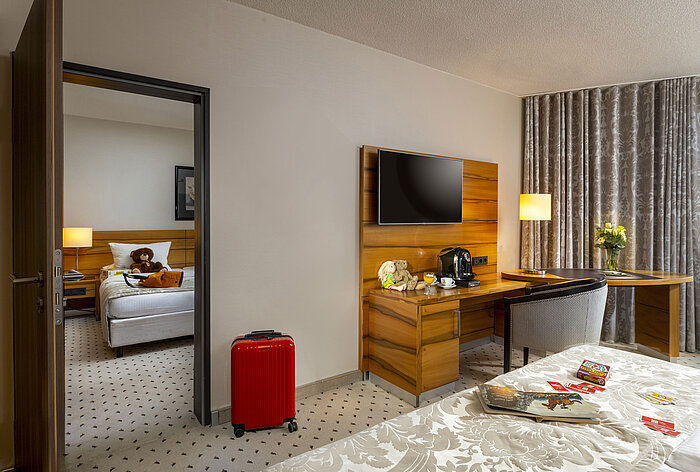 Habitación familiar en el Maritim Hotel Bad Homburg con cuarto separado para niños, ositos de peluche y maleta roja.
