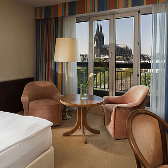Habitación superior en el Maritim Hotel Colonia con área de estar, cama cómoda y vista a la catedral de Colonia.