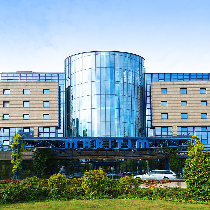 Vue extérieure de l'hôtel Maritim Bonn avec une façade en verre moderne et un jardin bien entretenu à l'avant.