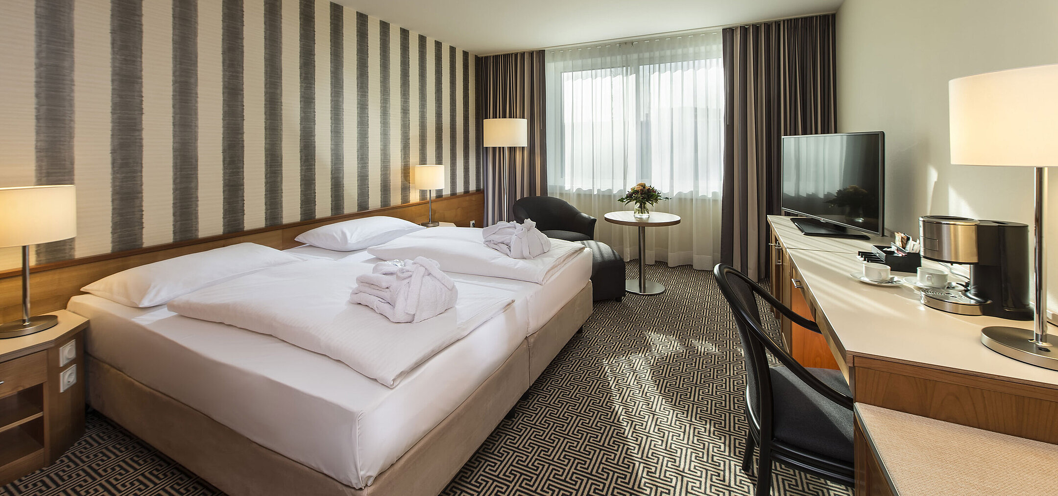 Chambre lumineuse avec bureau, fauteuils et grand lit à l’hôtel Maritim Stuttgart