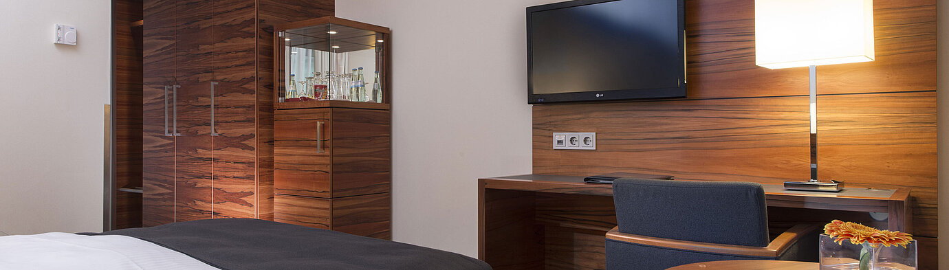 Chambre moderne au Maritim Hotel Munich avec espace de travail, TV, coin salon et grande armoire.