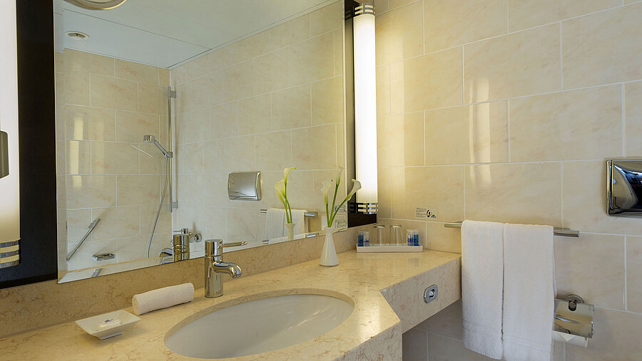 Baño moderno en el Maritim Hotel Fulda con lavabo de mármol, gran espejo y ducha a ras de suelo.