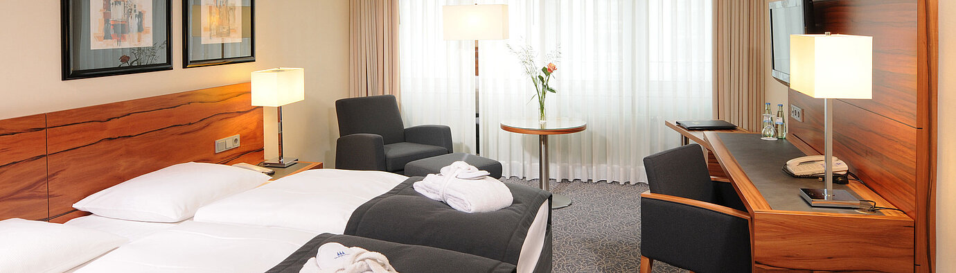 Chambre double lumineuse avec bureau, fauteuils et peignoirs à l’hôtel Maritim Munich