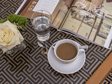 Gros plan sur rose, café, verre d’eau et magazine sur une table en verre