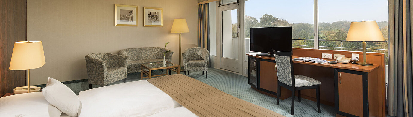Habitación confort del Maritim Hotel Kiel con acogedora zona de estar, escritorio, cama grande y maravillosas vistas al campo.