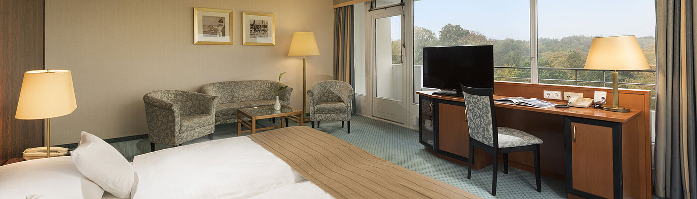 Comfort room at the Maritim Hotel Kiel with a cozy seating area, desk, large bed and a wonderful view of the countryside.