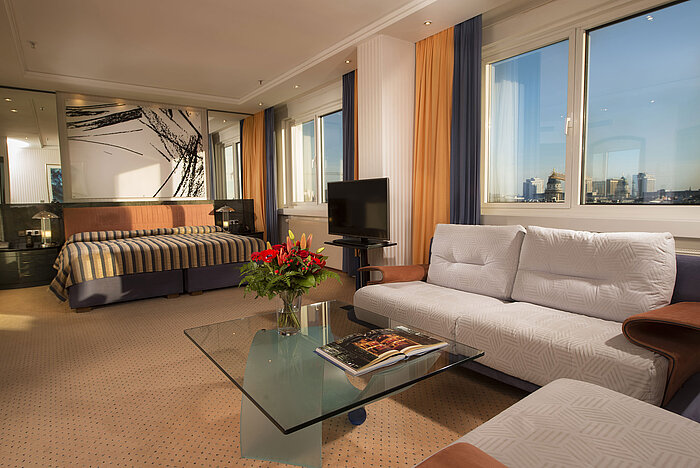 Suite Kuckei au Maritim proArte Hôtel Berlin avec canapé, table basse en verre et vue sur la skyline de Berlin.