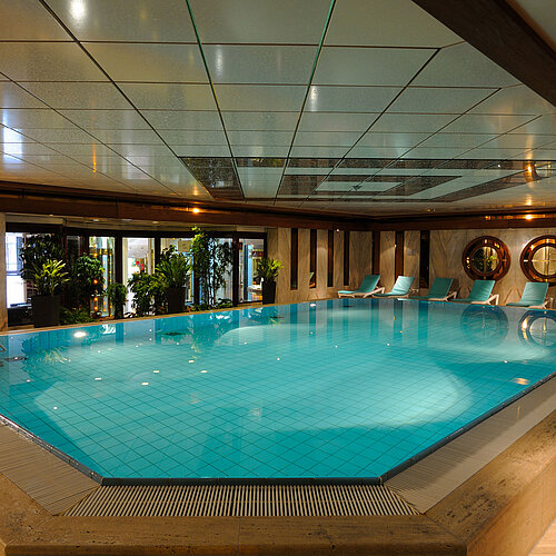 Piscine intérieure de l'hôtel Maritim Cologne avec chaises longues et plantes pour une ambiance relaxante.