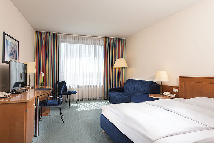 Camera classica al Maritim Hotel Frankfurt con letto matrimoniale, scrivania, divano e grandi finestre per luce naturale.