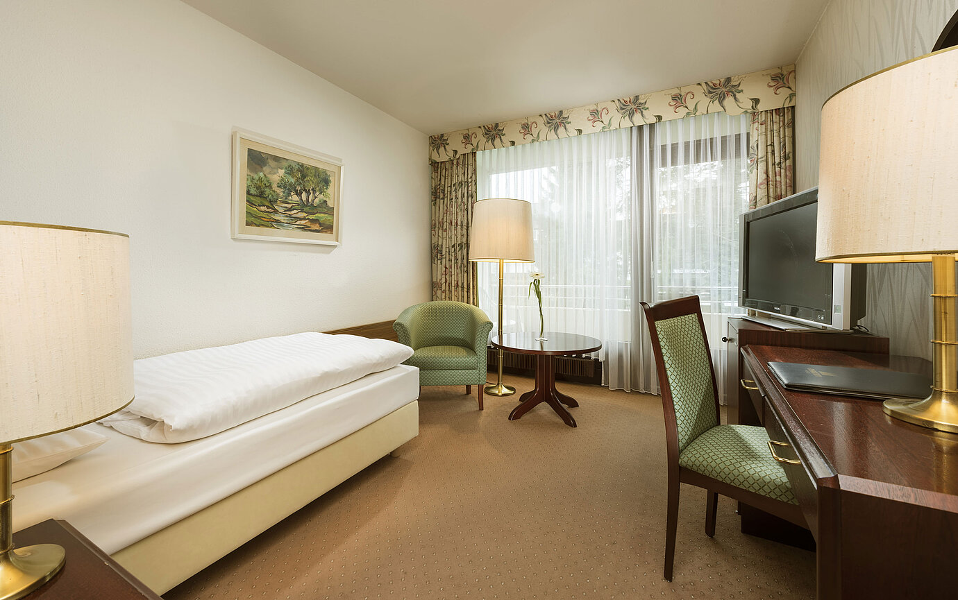Chambre avec fauteuil, bureau et accès au balcon à l’hôtel Maritim Bad Salzuflen