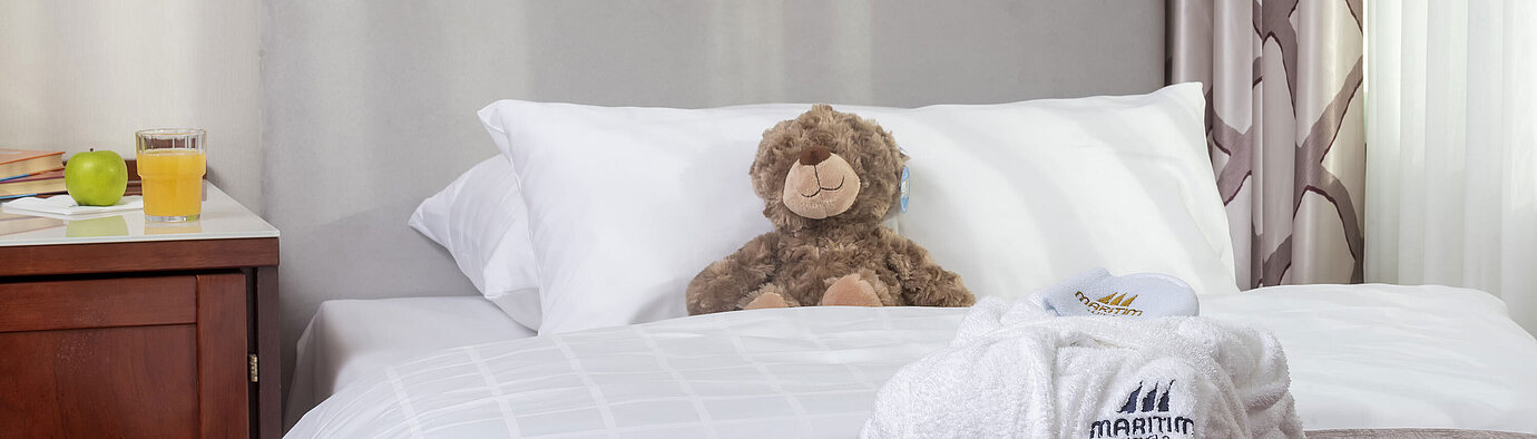 Family Suite Family suite at the Maritim Hotel Bonn featuring a cozy bed, stuffed toys, and a bathrobe, perfect for kids.