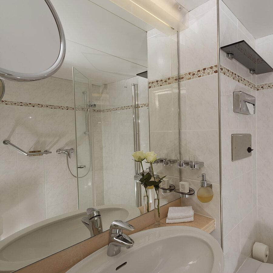 Baño luminoso en el Maritim Hotel Bad Salzuflen con ducha, espejo grande y azulejos blancos