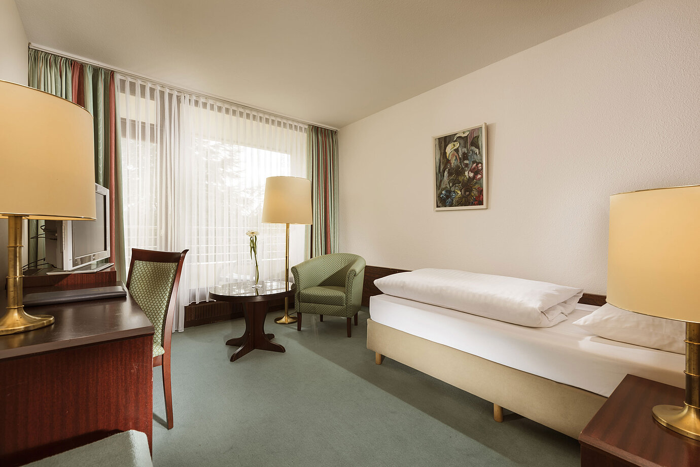 Chambre claire avec bureau, fauteuil et grande fenêtre à l’hôtel Maritim Bad Salzuflen
