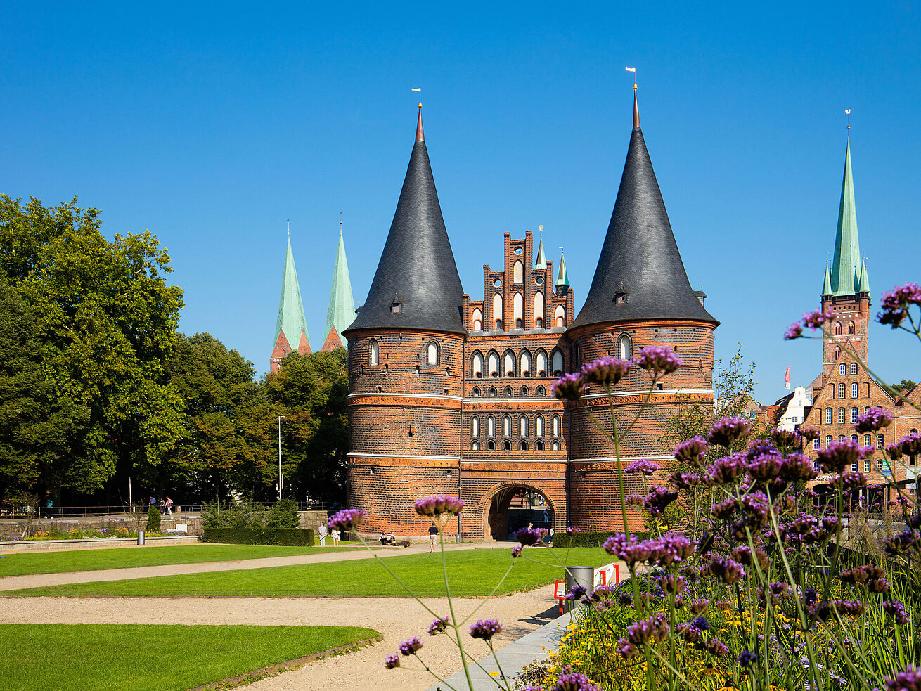 Holstentor a Lubecca con fiori in fiore in primo piano e cielo azzurro.