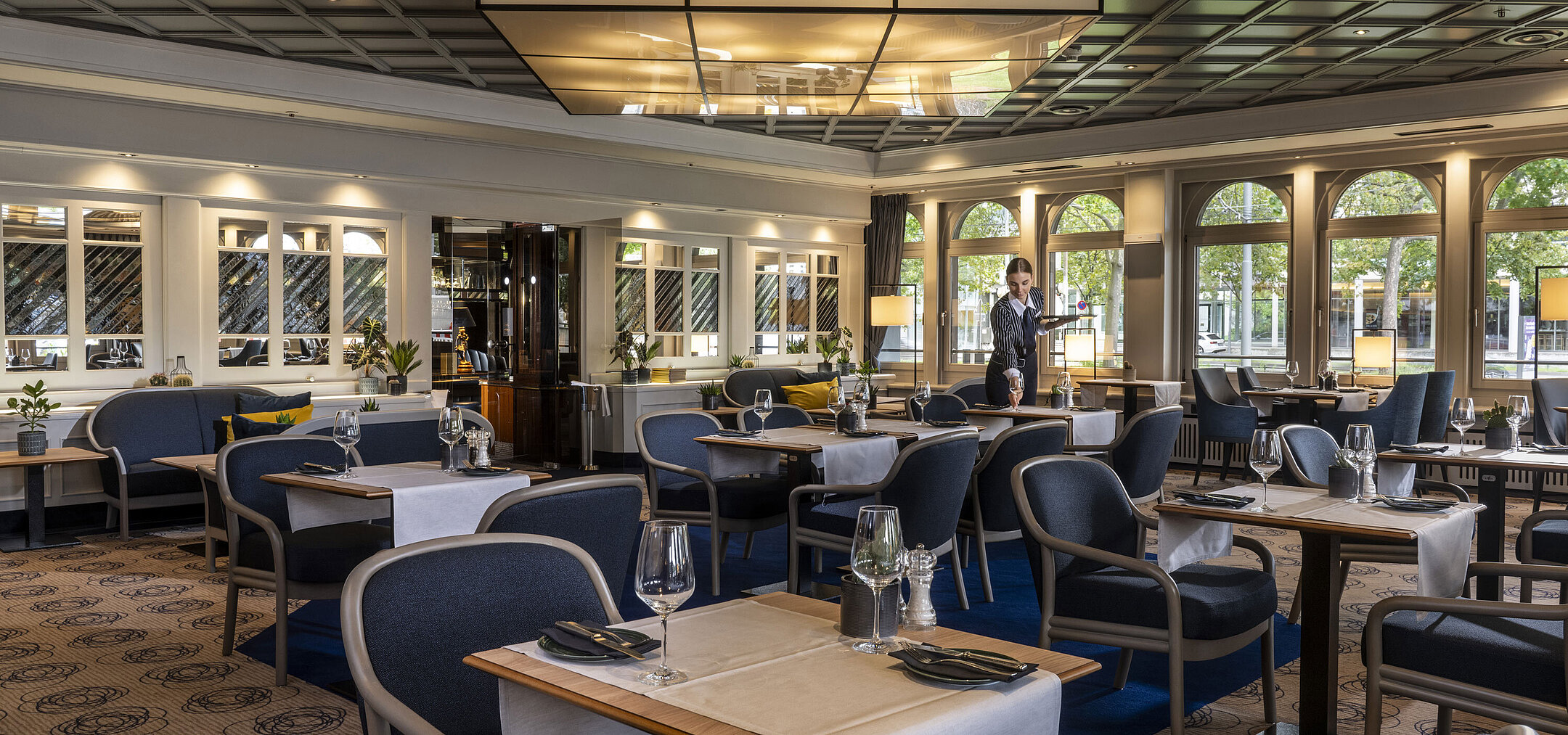 Restaurante moderno en el Hotel Maritim Darmstadt con mesas puestas y diseño elegante. Un empleado está brindando servicio.