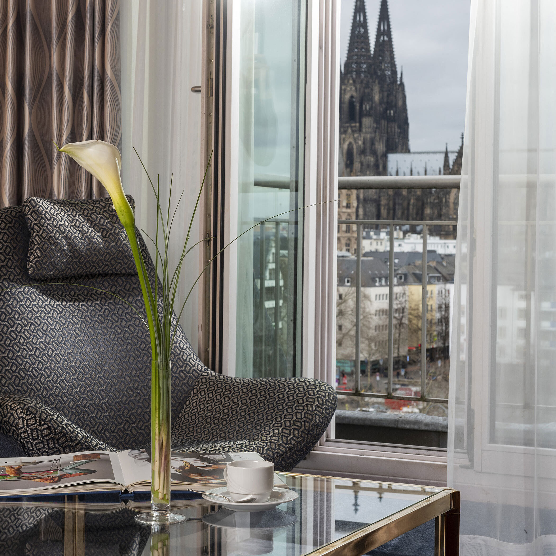 Suite Junior Junior Suite al Maritim Hotel Colonia con vista sul Duomo di Colonia, poltrona moderna e tavolino con decorazioni.